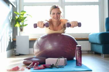 Genç bir kadın evde halterli halterlerle spor yapıyor. Ev sporları eğitimi ve sağlık