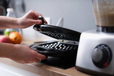 Woman opens electric waffle iron in kitchen. Cooking waffles in electric waffle iron concept