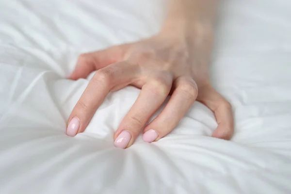 Woman hand tightly grips white sheet on bed. Nightmares and temper tantrums in the morning