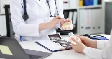 Female plastic surgeon shows silicone breast implant to patient. Augmentation and lifting of female breast and choice of implants