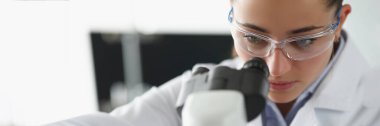 Kadın kimyagerin portresi laboratuarda mikroskop altında numune inceleniyor. Kadın bilim adamı materyali ve koruyucu üniformayı keşfeder. Laboratuvar kavramı