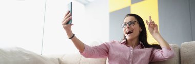 Güzel genç bir bayanın düşük açıyla barış işareti göstermesi ve akıllı telefondan selfie çekmesi. Video görüşmesinde arkadaş ya da aileyle konuş. Teknoloji, eğlence, eğlence konsepti