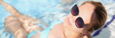 Havuzda son moda gözlük takan mutlu genç bir kadın manzarası. Tatilde rahatlatıcı bir atmosfer, güneşli bir gün. Tatil, tatil, otel, yalnız zaman kavramı.