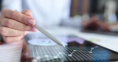 Bir kadın, tablet ekranında bir çizelgenin üzerinden kalemi hareket ettiriyor, yakın plan. İş kadını piyasayı inceliyor.