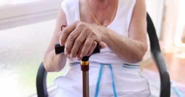 Yaşlı bir kadın bastona yaslanıyor, yakın plan, yüzeysel odaklanma. Yaşlılar için bakım evi, pasif dinlenme