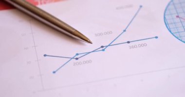 A silver metal pen lies on a diagram close-up. Comparison of financial indicators, traders workplace