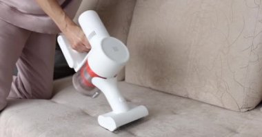 Dizlerinin üzerine çökmüş bir kadın kanepeyi temizliyor, yakın plan. Ev ödevi, döşenmiş mobilyaları temizleme, ev aletleri.