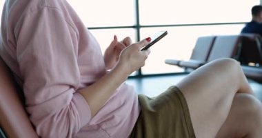 Kız, bekleme odasındaki bir sandalyede elinde akıllı bir telefonla oturuyor, yakın plan. Havaalanı terminali, yolcular