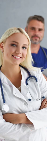 年轻微笑女子的画像在实习后在诊所开始全天工作 穿着制服的快乐的医生 身后的人支持着 帮助概念 — 图库照片