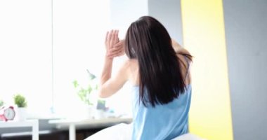 Uzun saçlı bir kadın yatakta otururken ellerini kaldırır. Sabah Uyanışı konsepti