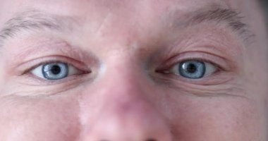 Young man with blue eyes is doing eye exercises. Male flirting technique concept