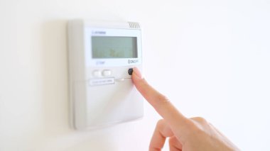 Wall mounted digital climate control and home thermostat. Female fingers set comfortable degrees of temperature adjustment in living room or hotel closeup