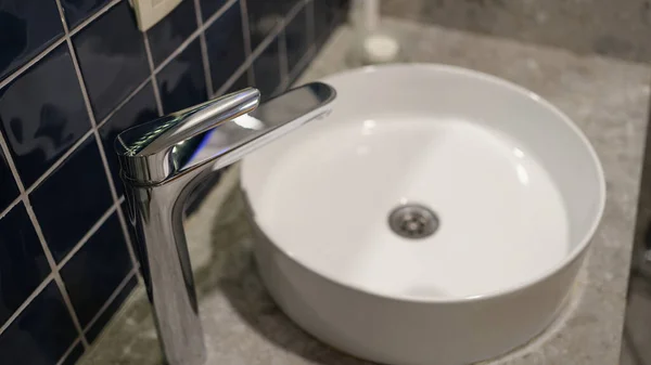 Washbasin and bathroom faucet detail of room interior. Chrome faucet and round porcelain washbasin concept