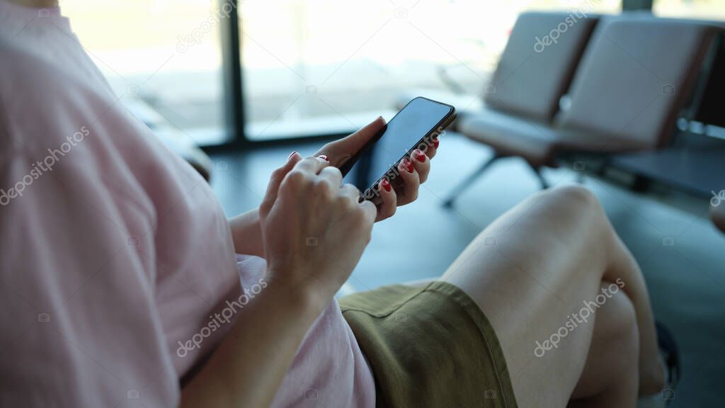 Woman traveler with smartphone in her hands sits in departure area at airport or train station. Application for gadgets of tourists or search for information for travelers concept