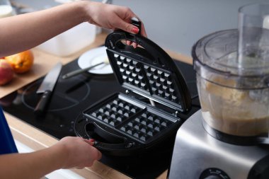 Woman has prepared Belgian waffle dough and opens electric waffle iron. Cooking homemade sweet tasty waffles concept