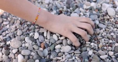 Genç bir el avuç içinden çakıl taşlarını alır, yakın plan. Kumsalda rahatla, terapi için taşlar, yavaş çekim