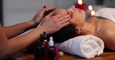 Masör, genç bir kadının yüzünü nazikçe okşar, yakın plan, yavaş çekim. Güzellik salonunda yüz bakımı