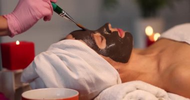 The cosmetologist applies a mask with a brush on the face of a lying woman, close-up. Chocolate face mask