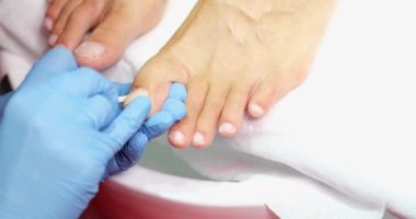 Pedicure master cleans nails from dry skin and dirt on toes with wooden stick. Hygiene and foot care in beauty salon