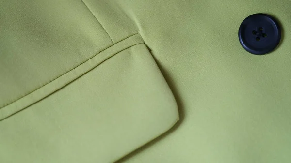 Closeup of green jacket with black button and pocket. Details of stylish green jacket