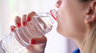Closeup of young woman drinking water from plastic bottle. Hydration concept and cooling thirst