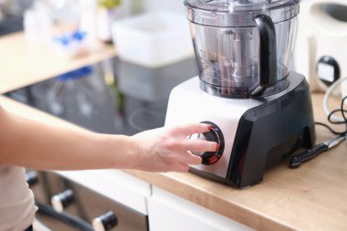 Woman switches button on electric blender in kitchen. Kitchen appliances for chopping and mixing food concept