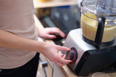 Woman turns on mixer with dough in kitchen. Kitchen appliances for chopping and mixing food