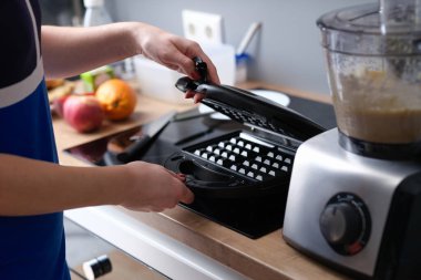 Person opens electric waffle iron in kitchen. Making Belgian waffles at home