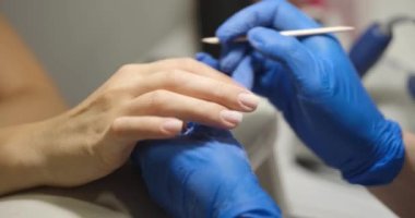 Hands of professional salon worker holding client hand while using cuticle pusher. Manicurist makes manicure in nail salon