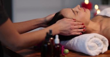 Woman feels happy and relaxes during face and head massage. Attractive beautiful girl lies on massage table receives physiotherapy from a masseuse for scalp care