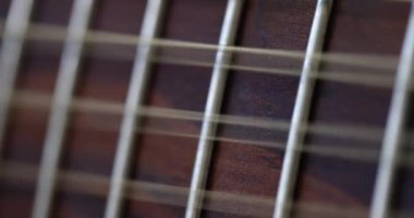 Closeup of acoustic guitar strings and the strings vibrate to reproduce melody of song. Stringed musical instrument that plays melody