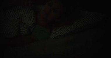Young woman in bed with alarm clock and open eyes suffers from insomnia and sleep disorder. Bright light prevents woman from sleeping