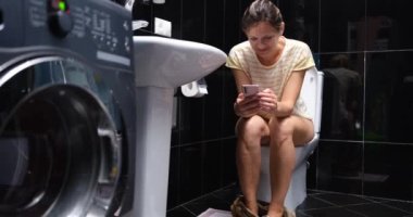 Happy young woman sitting on the toilet using mobile phone. Depend on phone or secret correspondence in love chat