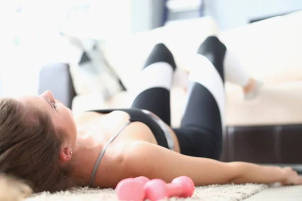 Tired woman lies on floor with dumbbells. Loss of motivation and sport goal concept
