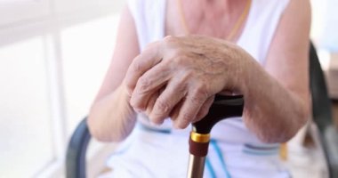 Old wrinkled hands lean on a wooden cane, shallow focus. Nursing home, quality care for the elderly, old age