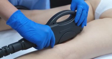 Cosmetologist removes hair on white legs with a laser, close-up. Beauty procedure in the salon, equipment