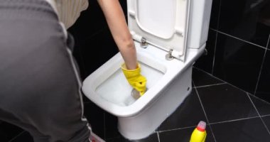 Woman brushing the toilet bowl at home, view from the back, close-up. Housework cleaning in bathroom
