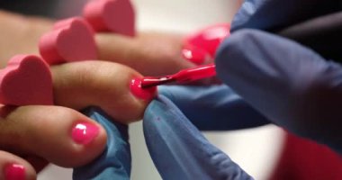 Pedicure master applies pink polish on toe nails, close-up. Cosmetic procedure in a pedicure salon