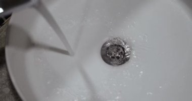 A stream of water flows from a tap into a white sink, close-up. Home plumbing equipment, washroom