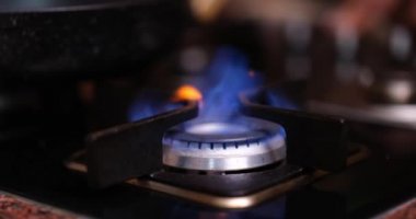 A gas burner on a brown stove burns with a blue flame, close-up. Cooking food in a frying pan, burning close-up