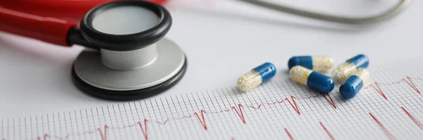 Medical capsules and red stethoscope lying on electrocardiogram closeup. Diagnostics and treatment of rhythm disturbances concept