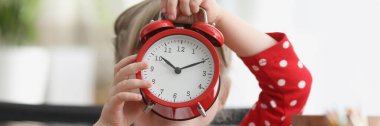 Küçük kız yüzünün önünde kırmızı alarmlı saati tutuyor. Çocuk konseptinde uyku ve uyanıklık