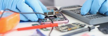 Usta tamirci cep telefonuna mikroçip yerleştiriyor. Cep telefonu onarımı ve servis kavramı