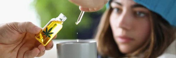 Drops of marijuana oil dripping into cup of sick woman wearing hat closeup. Cannabis addiction concept