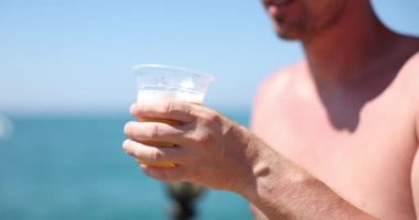 Young man drinking cold beer on summer beach. Handsome man enjoying a cold beer in the sultry heat of summer