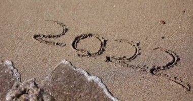 Inscription on sand 2022 is washed away by sea wave. End of 2022 and new year coming concept