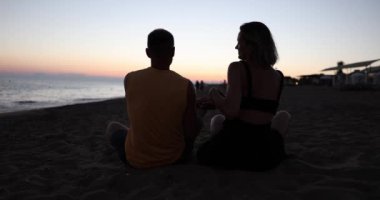 Husband and wife are sitting on beach daughter runs up to and hugs them at sunset. Family happy vacation and sea