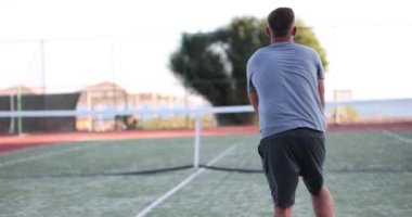 Rear view of young male tennis player during game or workout. Powerful hit of tennis player on ball on tennis court