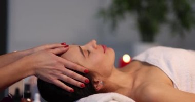 Woman with eyes closed and enjoys face and head massage in salon. Masseuse makes relaxing and therapeutic head massage