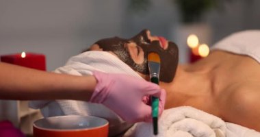 Spa worker applies clay mask to client faces using special tool. Moisturizing facial skin rejuvenation